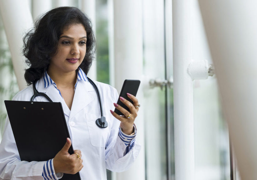 Attractive Asian health care professional reading text messages on a smart phone. Shot with telephone lens using shallow depth of field to blur out background details.